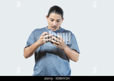 Surpris jeune homme jouant avec un téléphone cellulaire isolé. Joueur étonné jouant avec le téléphone cellulaire isolé Banque D'Images