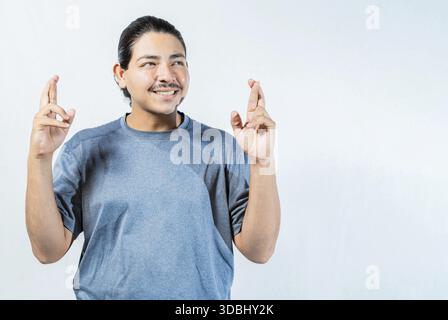 Homme plein d'espoir faisant un vœu avec les doigts isolés. Gars optimiste souriant et faisant un vœu isolé Banque D'Images