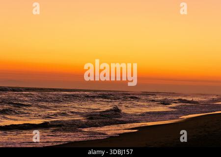 Coucher de soleil doré sur l'océan à Huntington Beach, Californie, avec des vagues ondulantes, un ciel chaud et un littoral calme le long de la côte. Banque D'Images