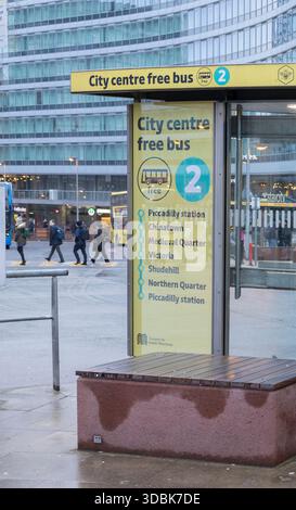 Manchester, royaume-uni, 19 janvier 2025 panneau d'arrêt de bus jaune vif avec un badge bleu '2', annonçant un service de bus gratuit. Installé contre un bâtiment en verre élégant, Banque D'Images