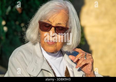 Portrait d'une femme âgée élégante aux cheveux blancs portant des lunettes de soleil à l'extérieur dans une lumière naturelle chaude. L'image représente le vieillissement gracieusement, confiez Banque D'Images