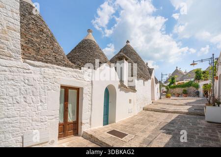 Vue d'une rue caractéristique des maisons Trulli à Alberobello, Pouilles, Italie. Comprend des toits coniques en pierre emblématiques et des plantes verdoyantes. Banque D'Images