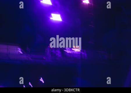 Un flou de mouvement abstrait de lumières de club ou de scène violettes et bleues, créant un fond de fête vibrant et énergique. Banque D'Images
