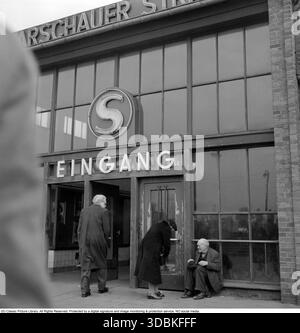 Entrée de la station Warschauer Straße, Berlin est (1957) cette photo de 1957 montre l'entrée extérieure (Eingang) de la station Warschauer Straße S-Bahn (et probablement U-Bahn) à Friedrichshain, Berlin est (Ostberlin). Le panneau lumineux « S » au néon marque le S-Bahn de Berlin – le réseau ferroviaire de banlieue de la ville – tandis que le bâtiment porte le nom de la gare « WarschauerStraße »). Dans la ville divisée de la guerre froide (quatre ans avant le mur de Berlin), il s'agissait d'un centre de transport clé reliant Berlin-est au reste du réseau, toujours exploité par la Reichsbahn est-allemande mais accessible des deux côtés. Les trains traversaient s Banque D'Images
