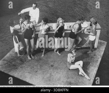 Au bar dans les années 1930 Une scène d'un bar en plein air avec des hommes et des femmes en maillots de bain. Le barman vêtu de blanc se verse dans un verre. Banque D'Images