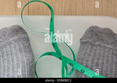 Pieds portant des chaussettes debout sur une balance numérique avec un ruban à mesurer vert Banque D'Images