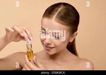 La femme examine soigneusement le sérum pendant le traitement de soin de la peau en studio. Elle se concentre sur le maintien d'une peau saine tout en utilisant des cosmétiques pour lueur et anti Banque D'Images