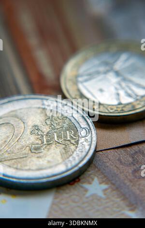 Deux pièces en euros sont sur une surface en bois. Une pièce montre clairement les détails, tandis qu'un billet de banque se trouve sous eux. Les pièces sont vues de près pendant da Banque D'Images