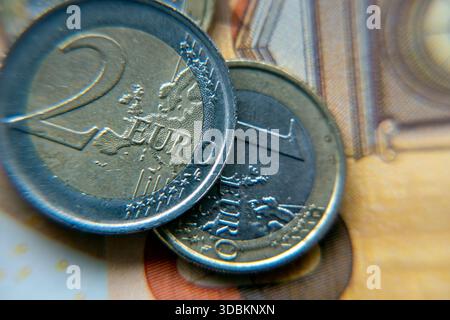 Vue rapprochée de deux pièces en euros et d'une pièce en euros reposant sur un billet de banque. L'image montre clairement les surfaces et les dessins des pièces de monnaie, mettant en évidence leurs caractéristiques. Banque D'Images