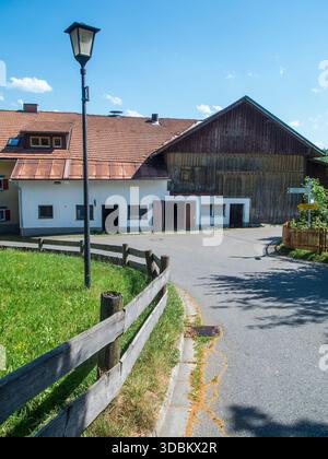 Vue idyllique sur le village avec grange résidentielle sur une branche de route en pente avec lanterne, clôture en bois et panneau indiquant Faistenoy. Banque D'Images