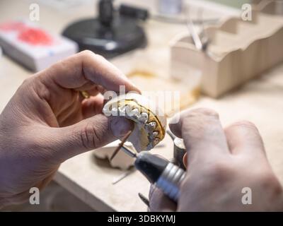 Technicien dentaire polissant la couronne dentaire en métal sur modèle en plâtre à l'aide d'un outil rotatif dans un laboratoire dentaire moderne. Banque D'Images