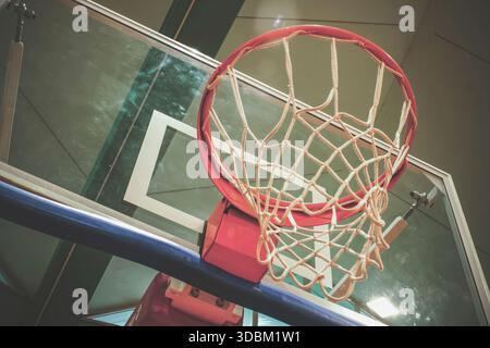Vue en angle bas d'un panier de basket-ball et filet suspendu sur un panneau transparent dans un gymnase bien éclairé, prêt pour le match Banque D'Images
