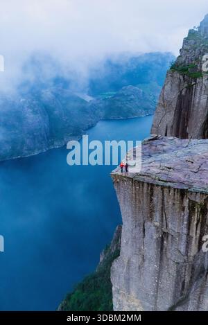 Deux courageux aventuriers se tiennent au bord de la falaise Preikestolen, surplombant les eaux sereines du Lysefjorden. Banque D'Images