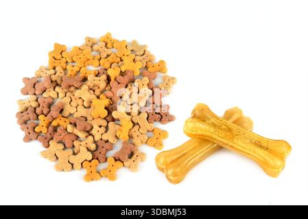 Une variété de biscuits colorés en forme d'os pour chiens sont empilés à côté de deux grandes friandises en cuir brut. Cette prise de vue à angle élevé offre un grand espace de copie Banque D'Images