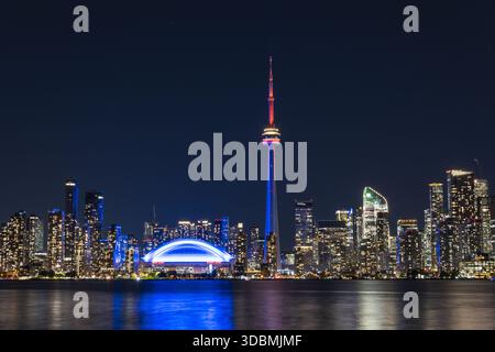 Vue aérienne de la Tour CN et du Centre Rogers brillent brillamment contre le ciel nocturne, reflété dans les eaux tranquilles, Toronto, Ontario, Canada. Banque D'Images