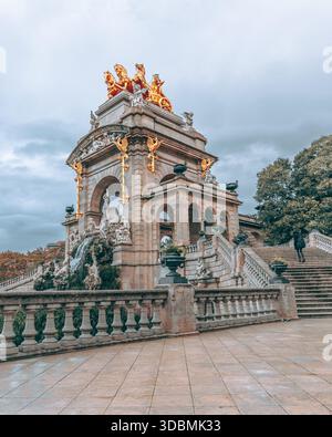 Vue d'un char doré au sommet d'une fontaine de pierre avec de grands escaliers sous un ciel nuageux, un monument historique, Barcelone, Catalogne, Espagne. Banque D'Images