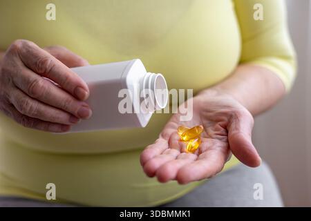Mains seniors versant des capsules dorées à partir du pot de pilule blanc. Santé à l'âge adulte, maintien de l'activité et de l'énergie. Prévention des maladies, utilisation de vitamines an Banque D'Images