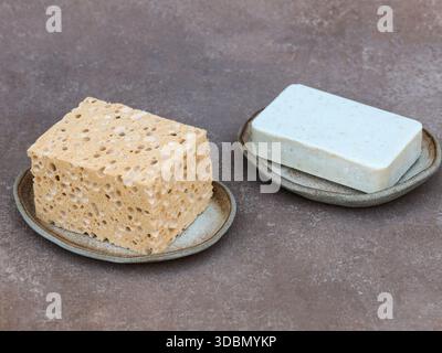 Nature morte minimaliste de pain de savon naturel et d'éponge de cellulose placés sur des porte-savons en céramique faits à la main. Scène de salle de bain calme avec des matériaux organiques, neu Banque D'Images