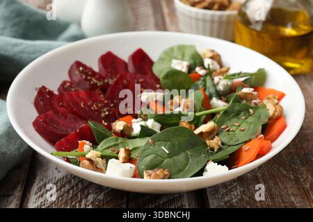 Délicieuse salade avec betterave, épinards, fromage, noix et carotte sur table en bois, gros plan Banque D'Images