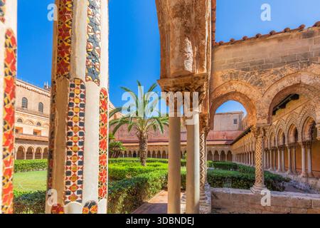 Détail du cloître bénédictin de Monreale, avec des colonnes en mosaïque décorées, des chapiteaux sculptés, des arches en pierre et des palmiers dans le jardin central. Un chef-d'œuvre de l'architecture normande dans la ville métropolitaine de Palerme, Sicile, Italie Banque D'Images