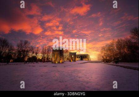 L'ancien temple égyptien de Debod couvert de neige pendant le coucher du soleil, brillant sous un ciel orange spectaculaire à Madrid. Banque D'Images
