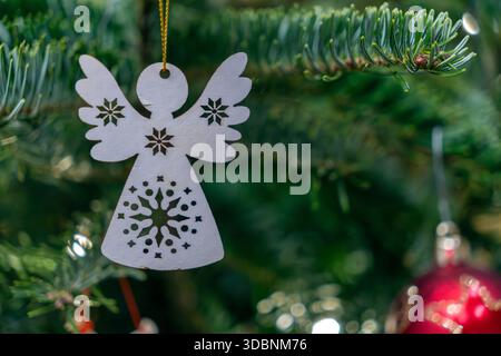 Un ornement ange avec des motifs découpés est suspendu à une branche de sapin de Noël. Des aiguilles vertes l'entourent, et une boule rouge est également visible dans le backgrou Banque D'Images