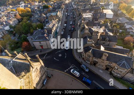 Vue aérienne panoramique de Peebles High Street capturant des voitures, des façades en pierre et du feuillage d'automne. Banque D'Images