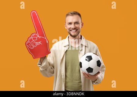Ventilateur de football masculin avec balle et main de mousse sur fond orange Banque D'Images
