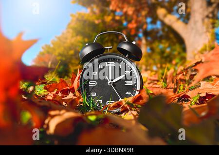 Alarm clock between autumn leaves, symbol photo time change and winter time Banque D'Images