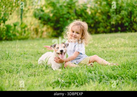 Joyeuse petite fille embrassant jack russell terrier chien sur la pelouse d'herbe verte - l'amitié pour les animaux de compagnie de l'enfant Banque D'Images