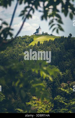 Vue de l'église de la préparation Primoz près de Jamnik en Slovénie. L'église est idyllique sur une crête légère dans une forêt dense. Banque D'Images