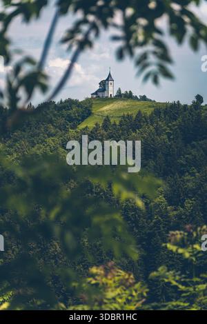 Vue de l'église de la préparation Primoz près de Jamnik en Slovénie. L'église est idyllique sur une crête légère dans une forêt dense. Banque D'Images