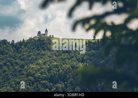 Vue de l'église de la préparation Primoz près de Jamnik en Slovénie. L'église est idyllique sur une crête légère dans une forêt dense. Banque D'Images