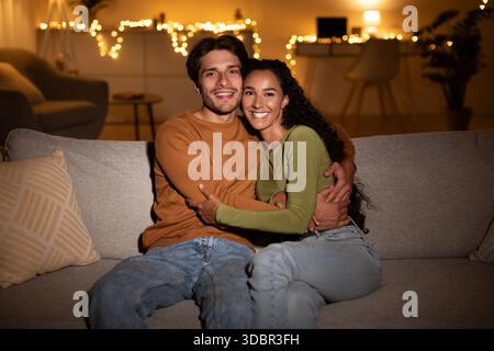 Heureux couple profitant d'une soirée confortable ensemble sur leur canapé à l'intérieur Banque D'Images