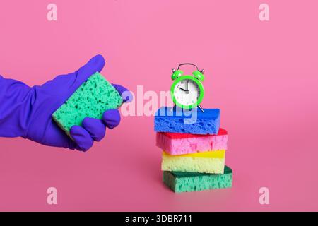 mains dans le gant en caoutchouc violet pressant l'éponge verte sur le concept de nettoyage de fond rose pastel isolé Banque D'Images