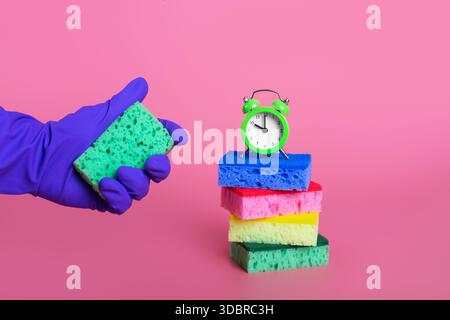 mains dans le gant en caoutchouc violet pressant l'éponge verte sur le concept de nettoyage de fond rose pastel isolé Banque D'Images