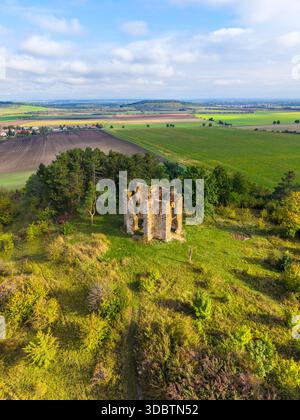 Le drone capture les vestiges de la chapelle de l'exaltation de la Sainte-Croix à Bristev, entouré de verdure luxuriante et de terres agricoles sous un ciel bleu clair, mettant en valeur la nature reprenant l'histoire. Banque D'Images