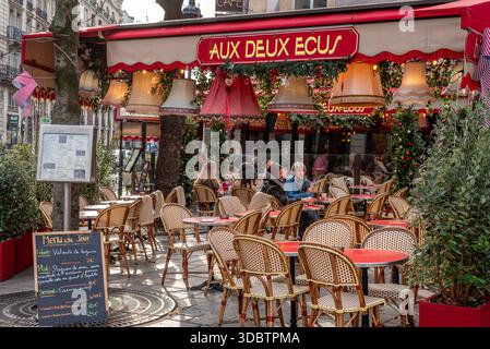 Personnes assises sur le patio extérieur d'une brasserie du 1er arrondissement de Paris. Abat-jour de différentes couleurs suspendus à l'extérieur d'un restaurant Banque D'Images