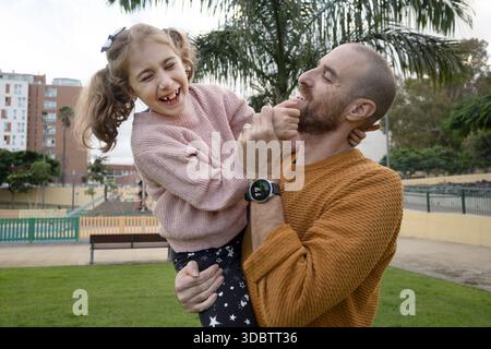 Père tenant sa fille et partageant un moment heureux au parc Banque D'Images