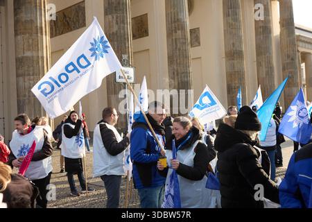 Berlin, Allemagne, 18 décembre 2025. Les employés du secteur public et les membres de la DPolG (Deutsche Polizeigewerkschaft) se rassemblent pour une grève et un rassemblement de protestation à grande échelle à la porte historique de Brandebourg. Des manifestants portant des gilets promotionnels blancs et portant de grands drapeaux syndicaux blancs et bleus se tiennent devant les colonnes emblématiques de Pariser Platz. Les participants s'engagent dans des discussions pendant la manifestation pour de meilleures conditions de travail, des salaires équitables et des réformes de la fonction publique. Cette image d'archive documente l'activisme syndical dans la capitale allemande. Crédit : Felix Wolf/Alamy Live News Banque D'Images