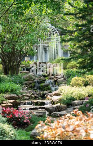 Superbe vue sur le jardin tropical avec une cascade rocheuse en gradins menant à un grand belvédère blanc de style cage à oiseaux. Entouré de verdure luxuriante et vibran Banque D'Images
