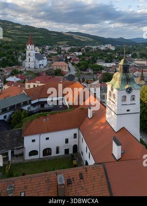 Vue aérienne de la lumière du soleil baignant les toits en terre cuite des bâtiments historiques, contrastant avec les collines verdoyantes au-delà, Gelnica, région de Kosice, Slov Banque D'Images