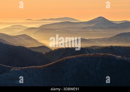 Vue aérienne des collines ondulantes et des montagnes nappées de teintes or et bleu sous un ciel pastel, Mala Fatra, région de Zilina, Slovaquie. Banque D'Images