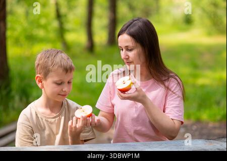 Mère et fils mangeant des pommes, souriant et partageant des fruits dans le parc Banque D'Images