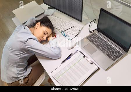 Femme d'affaires fatiguée dormant au bureau avec ordinateur portable, paperasse et burnout Banque D'Images