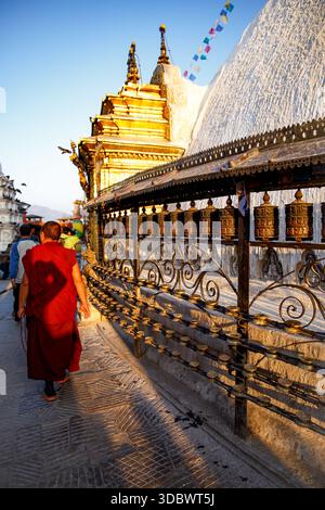 Un moine bouddhiste passe devant des roues à prières à Boudhanath Stupa tandis qu'un touriste marche devant Katmandou, au Népal. Banque D'Images