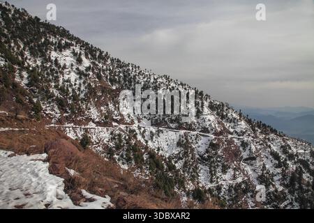 Vue sur les feuilles persistantes enneigées accrochées aux pentes escarpées, une route sinueuse serpente à travers le paysage hivernal, une vue sereine, Muzaffarabad, Az Banque D'Images
