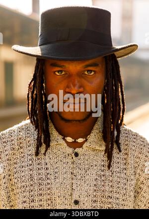 Un homme avec des dreadlocks et un chapeau noir regarde directement la caméra. Banque D'Images