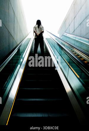 Une personne avec des dreadlocks se tient sur un escalier roulant, les mains derrière le dos. Banque D'Images