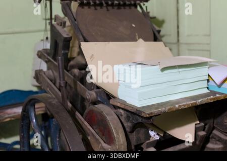 Une presse à imprimer se trouve dans un atelier avec des piles de papier prêtes à l'emploi. Banque D'Images